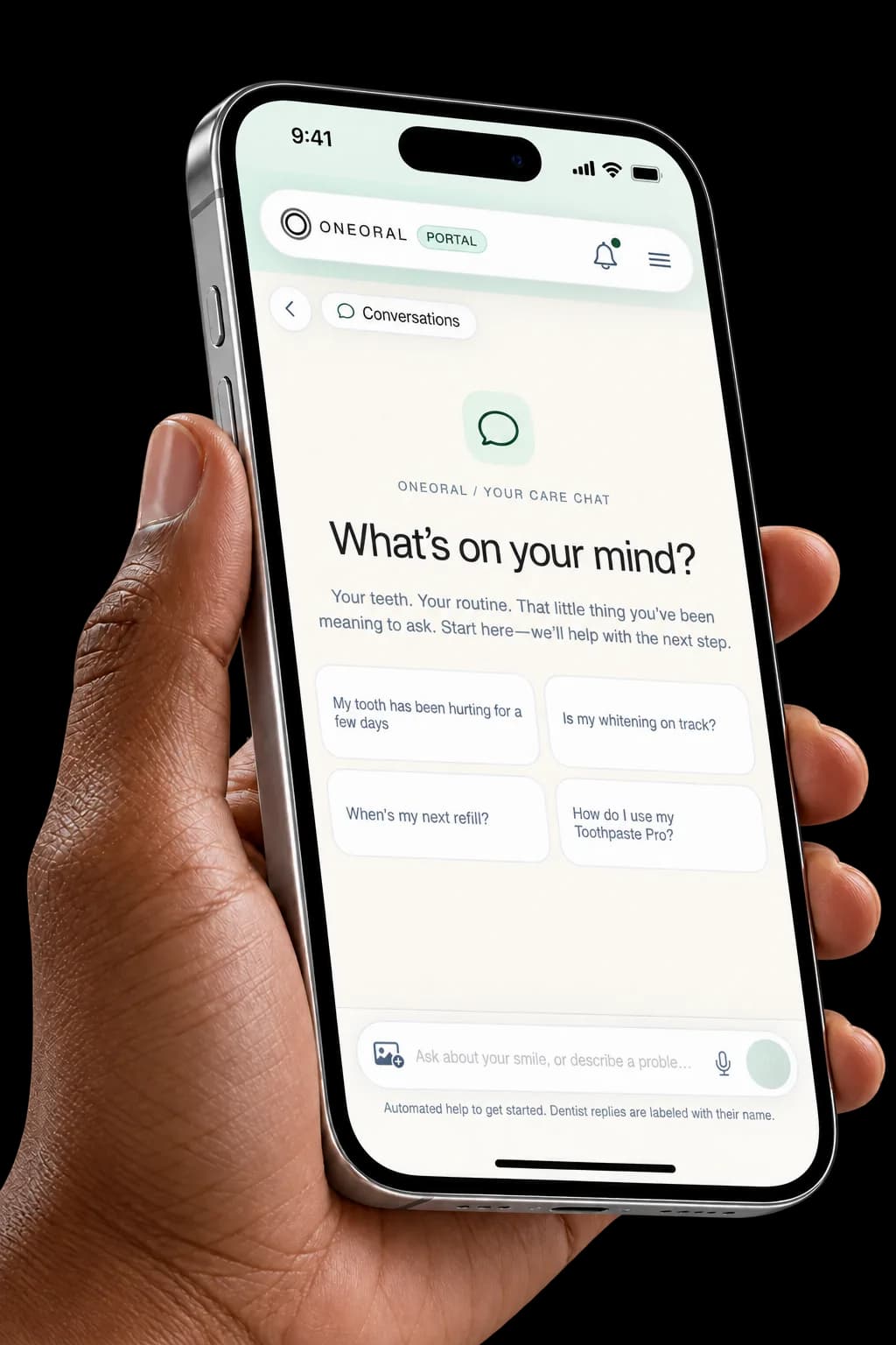 A brown hand holds a silver phone showing the OneOral portal care-chat welcome screen and suggested questions