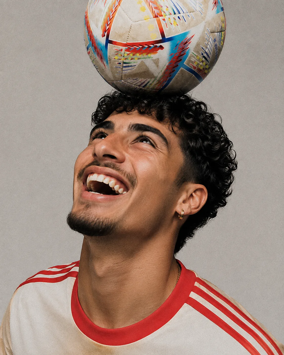 A footballer laughing, balancing a ball on their head