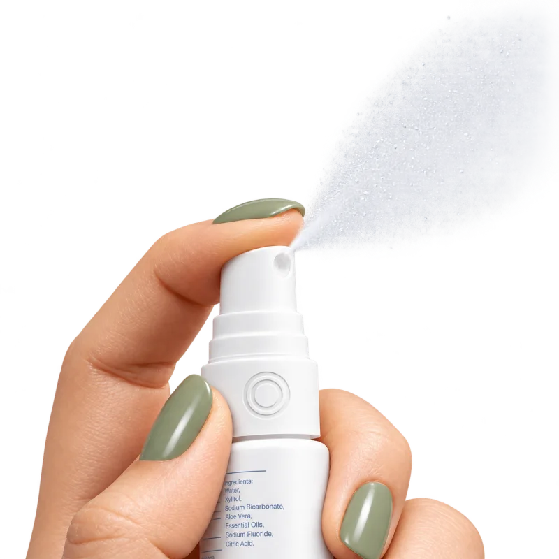 A hand pressing the oral spray, a fine mist leaving the nozzle